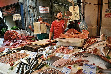 Un venditore in una bancarella piena di pesce fresco al mrcato del pesce di Palermo.