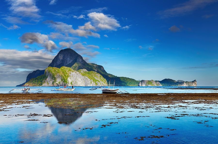 Veduta di El Nido e Cadlao a bassa marea con barche e montagne riflettenti.