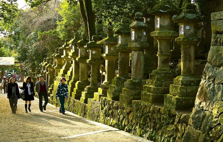 Turisti camminano accanto a lanterne di pietra con muschio al santuario Kasuga Taisha, Nara.