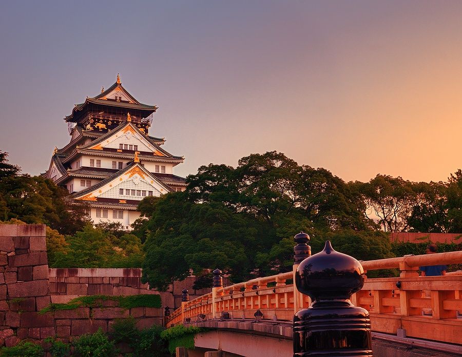 Osaka Castle al tramonto, con un ponte in primo piano e alberi circostanti.