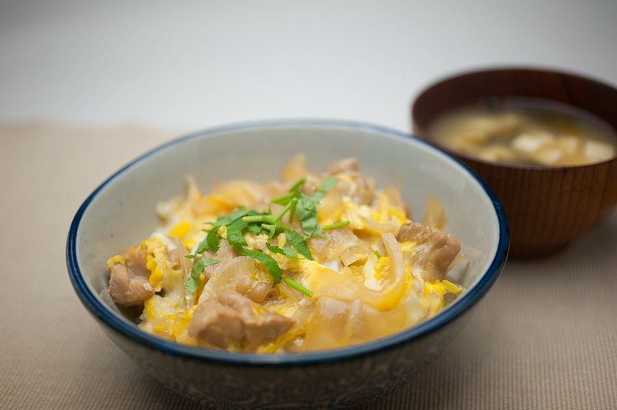 Oyakodon giapponese con pollo, uova e cipolle affettate, servito in una ciotola decorata.