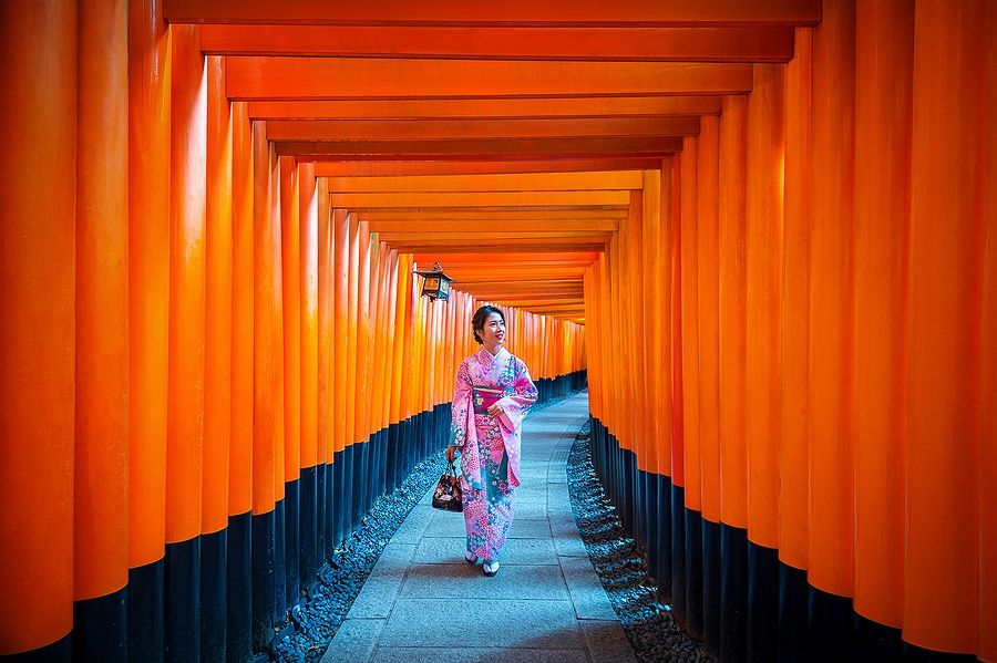 Donna in kimono al Fushimi Inari Shrine di Kyoto tra torii rossi.