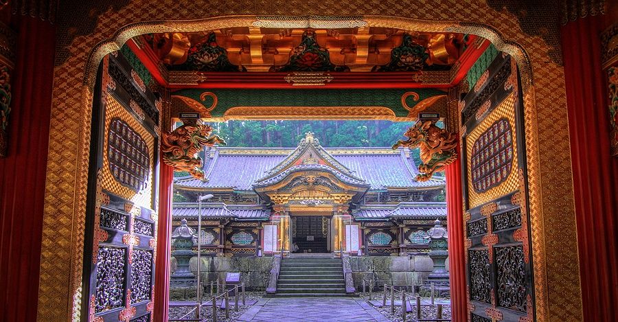 Ingresso del tempio Nikko con dettagli decorativi e un edificio tradizionale sullo sfondo.