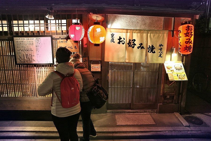Due persone fuori da un ristorante a Pontocho, Kyoto, illuminate da lanterne tradizionali.