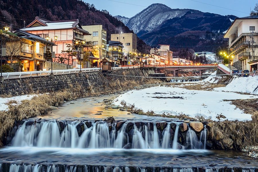 Ruscello serale a Shibu Onsen, Nagano, con edifici e montagne innevate.