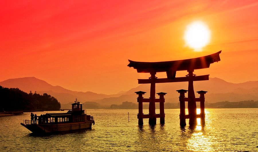 Torii Gate al tramonto con barca sullo sfondo a Miyajima, Giappone.