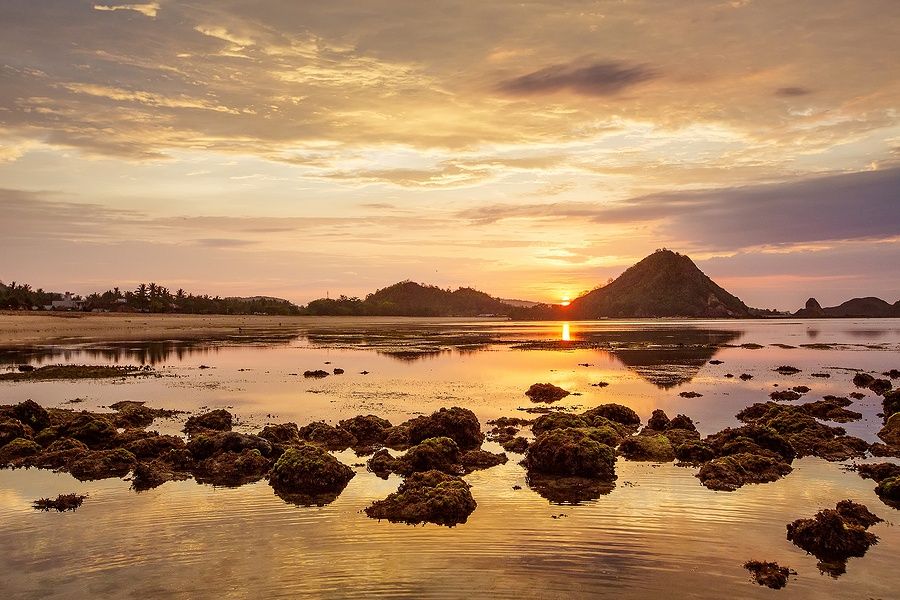 Tramonto sull'oceano Indiano a Lombok, Indonesia, con colline e mare calmo.