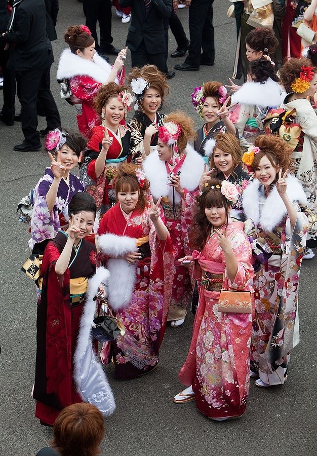 Donne giapponesi in kimono colorati sorridono e posano con il segno di pace.