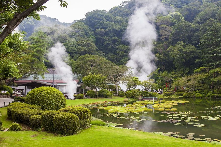 Sorgenti termali di Beppu con vapore che sale, circondate da vegetazione lussureggiante.