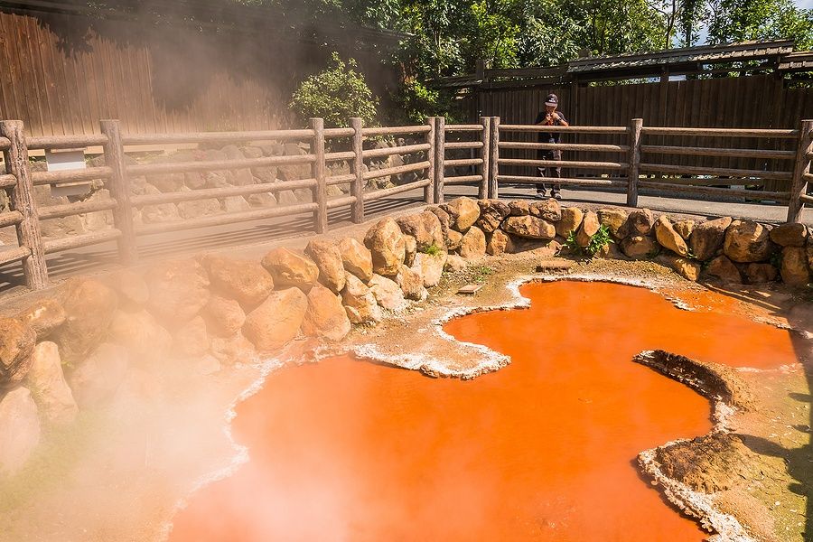 Pozza bollente rossa a Kamado Jigoku, Beppu, con staccionata e uomo.