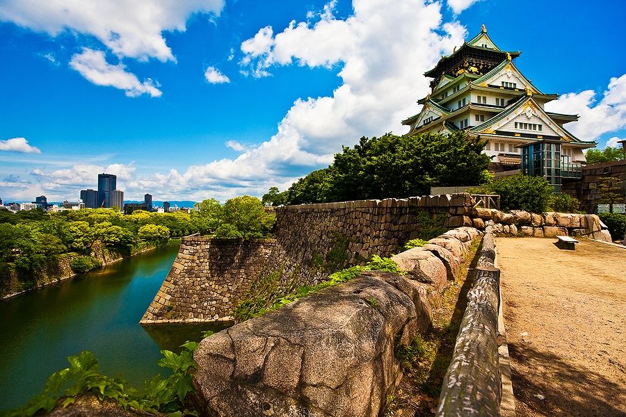 Castello di Osaka con cielo azzurro, nuvole bianche e giardini verdi.