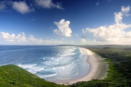 Spiaggia di Byron Bay in Australia con onde e vegetazione costiera verde.