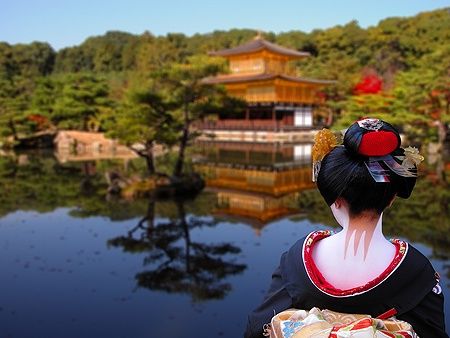 Una geisha guarda il tempio Kinkaku-ji a Kyoto, riflesso nel lago.