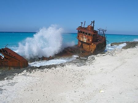 Un relitto arrugginito su una spiaggia di Bimini con onde che si infrangono.
