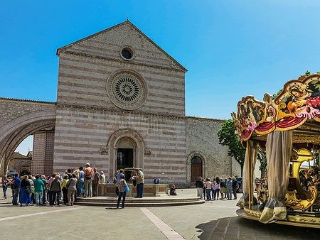 Facciata della Basilica di Santa Chiara ad Assisi con giostra e gruppo di persone.