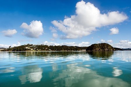 Paesaggio della Bay of Islands in Nuova Zelanda con nuvole e riflessi sull'acqua.
