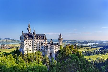 Castello di Neuschwanstein tra le colline verdi di Baviera sotto un cielo azzurro.