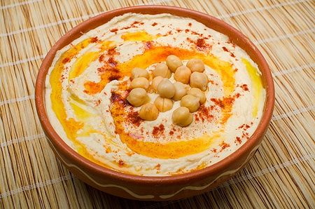 Ciotola di hummus con ceci, peperone rosso e olio d'oliva su tappetino di bambù.