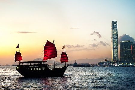Junk turistico nel Victoria Harbour di Hong Kong al tramonto con lo skyline dell'ICC.