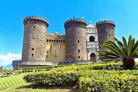 Il Maschio Angioino a Napoli con cielo azzurro e vegetazione.