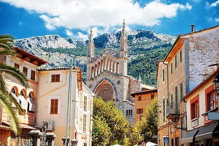 Vista della Cattedrale di Sant Bartomeu a Sóller, Mallorca, circondata da edifici pittoreschi e montagne.