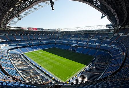 Vista interna dello stadio Santiago Bernabéu con tribune vuote e campo verde.
