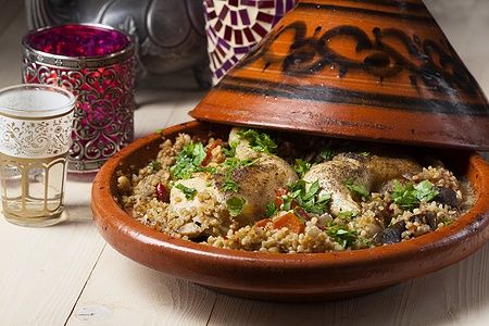 Tajine di pollo con couscous e zucchine in piatto di terracotta.