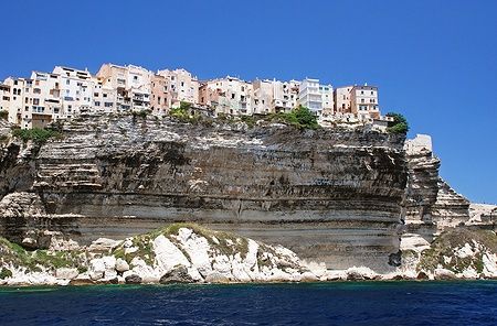 Edifici storici di Bonifacio su scogliere calcaree con mare blu.