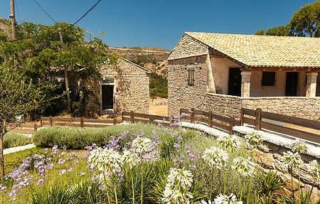 Casa tradizionale di pietra nel villaggio di Perithia, Corfù, con fiori e cielo azzurro.