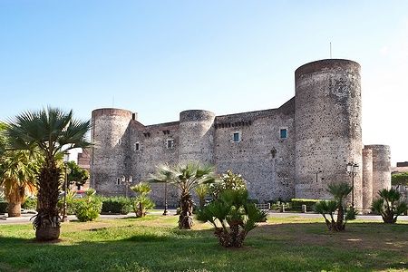 Castello Ursino a Catania circondato da palme e cielo blu.