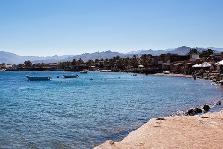 Vista del litorale di Dahab in Egitto, con mare, barche e persone che nuotano.