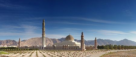 Grande Moschea del Sultan Qaboos a Muscat, con minareti e montagne sullo sfondo.