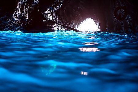 Interno della Grotta Azzurra a Capri, acqua blu luminosa e barca in silhouette.