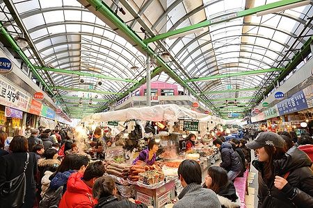 Folla nel Gwangjang Market di Seoul con bancarelle di cibo tradizionale.