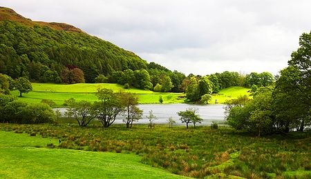 Paesaggio del Lake District con prati verdi e un lago.