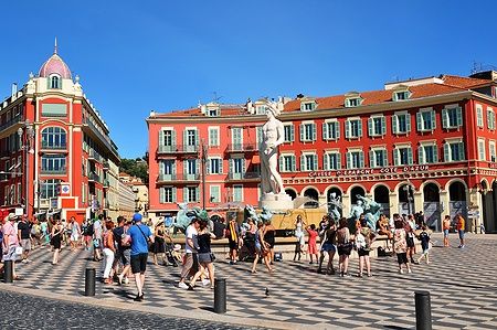 Turisti passeggiano a Place Massena a Nizza sotto il sole estivo.