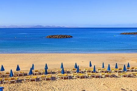 Spiaggia di Playa Blanca con ombrelloni blu e lettini gialli al mattino presto.