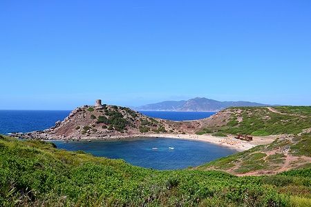 Spiaggia di Porticciolo in Sardegna con torre medievale e promontorio roccioso.