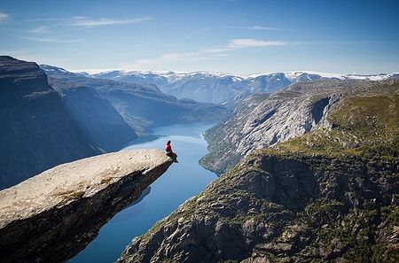 Uomo seduto su Trolltunga in Norvegia, con vista panoramica sul fiordo.