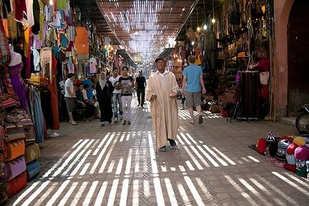 Uomo nel souk di Marrakech chiede l'elemosina tra passanti e venditori.