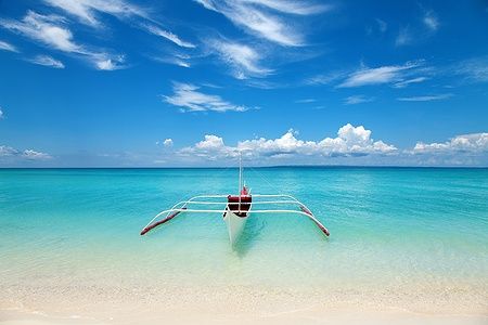 Barca bianca su una spiaggia tropicale con mare turchese e cielo blu.