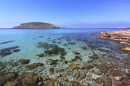 Spiaggia di Cala Conta a Ibiza con acque cristalline e isola sullo sfondo.