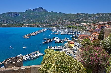 Vista panoramica di Calvi, Corsica, con porto, barche e montagne sullo sfondo.