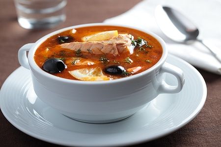 Fish solyanka, zuppa russa con salmone, olive e limone in ciotola bianca.