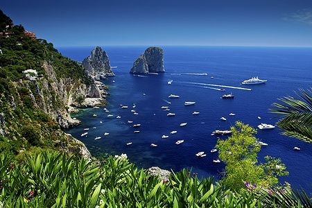 Vista dai Giardini di Augusto a Capri con mare blu, barche e Faraglioni.