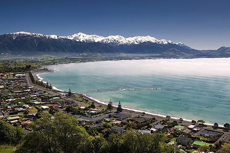 Vista di Kaikoura, Nuova Zelanda, con montagne innevate e nebbia lungo la costa.