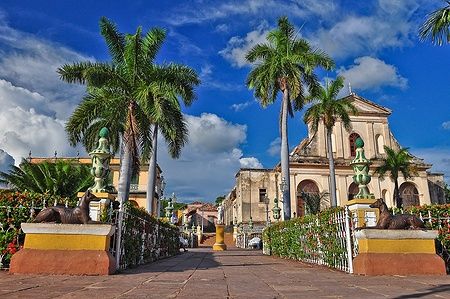 Plaza Mayor di Trinidad a Cuba con chiesa e palme sotto un cielo azzurro.