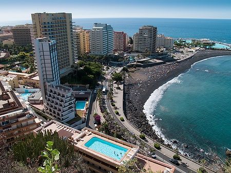Vista delle spiagge e hotel di Puerto de la Cruz, Tenerife con sabbia scura e mare azzurro.