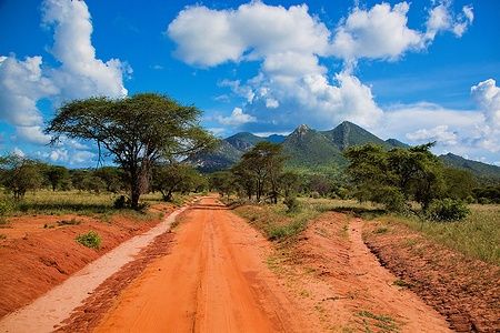 Strada di terra rossa attraverso la savana con montagne sullo sfondo in Tsavo West, Kenya.