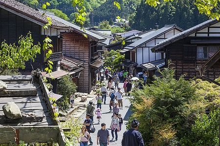 Persone passeggiano tra edifici in legno tradizionali in una strada di Tsumago, Giappone.